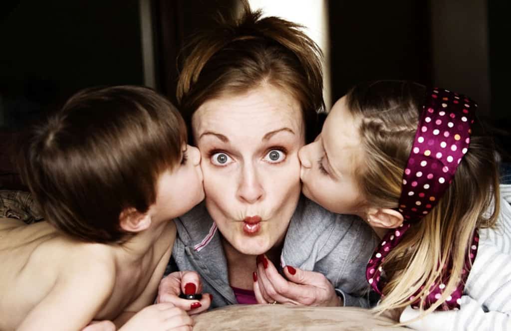 Mom with puckered lips being kissed by her kids