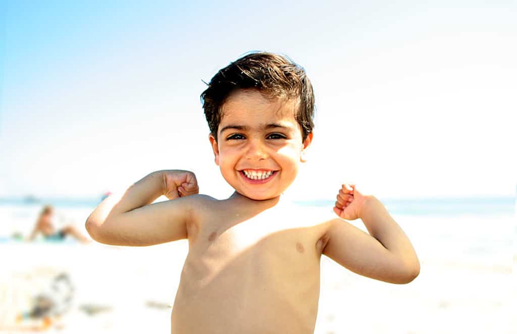Little boy showing his muscles on the beach