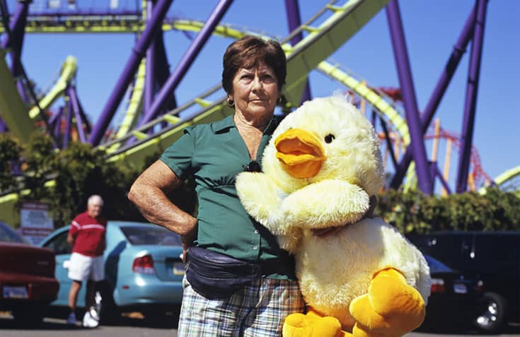 Grandmother holding stuffed duck at amusement park, not looking amused.