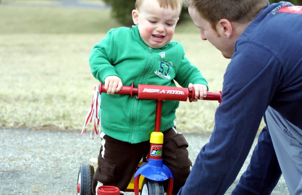 Toddler frustrated riding tricycle with patient father
