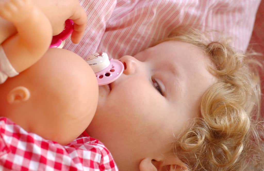 Sleepy toddler girl in bed with baby doll